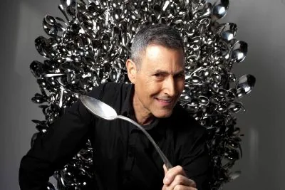 Uri Geller holding a spoon in front of a wall of spoons